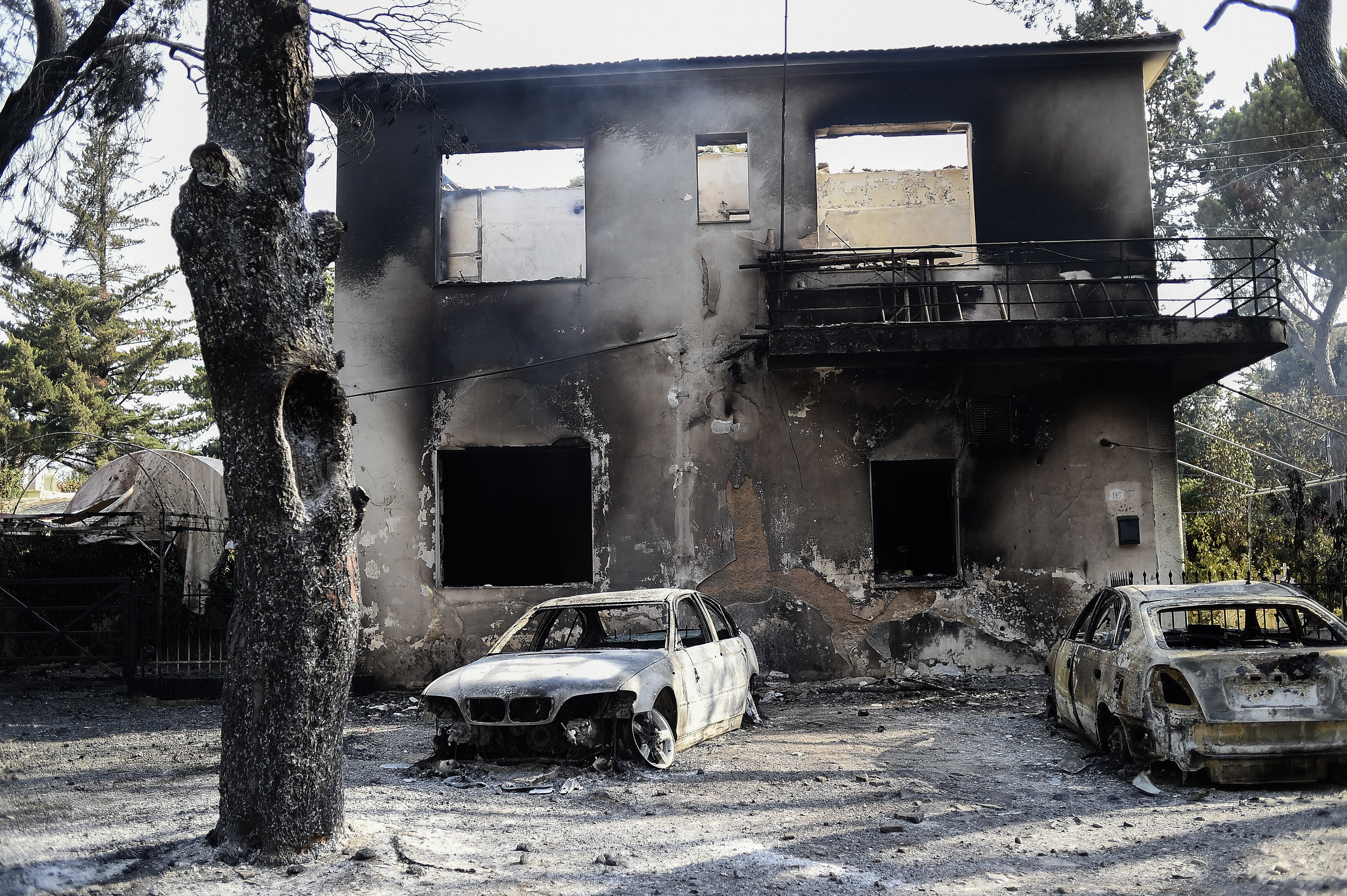 A burned out home with two destroyed vehicles in front