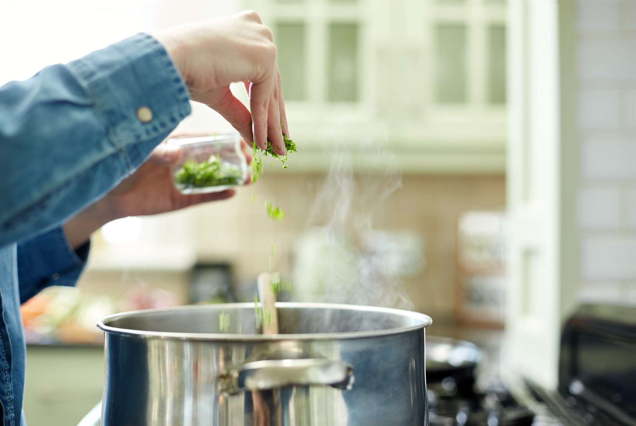 A woman sprinkling cilantro into a pot.