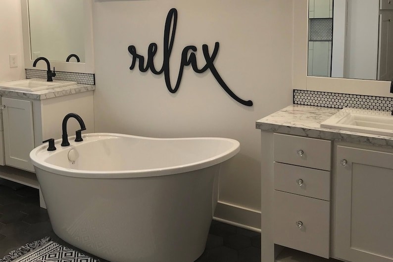 the word relax in lowercase cursive on a wall over a bathtub