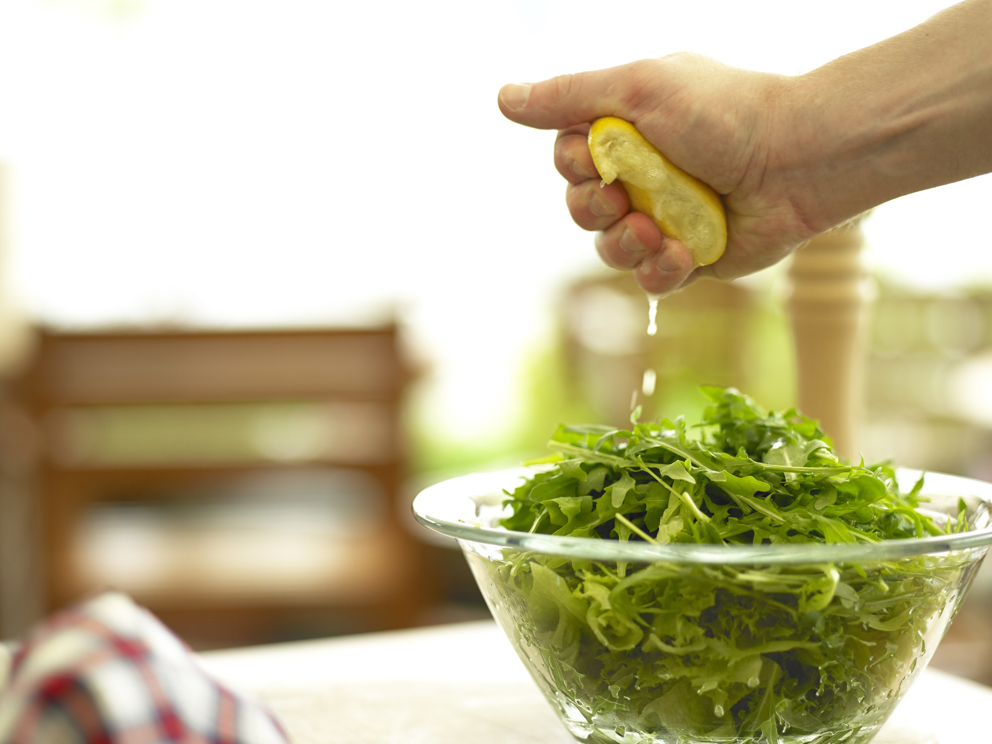 Squeezing lemon into a bowl of arugula.