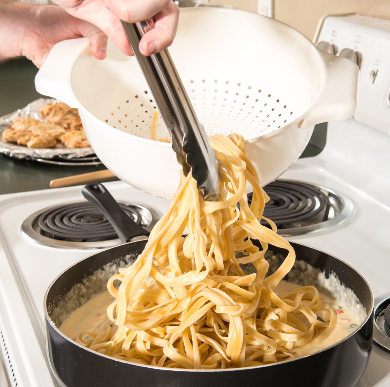 Placing fettuccine into a pan of cream sauce.