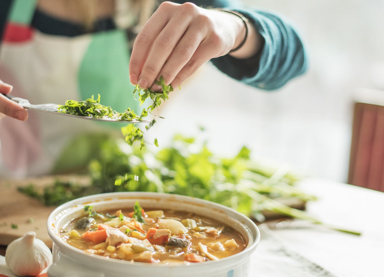 A woman sprinkling herbs into soup.