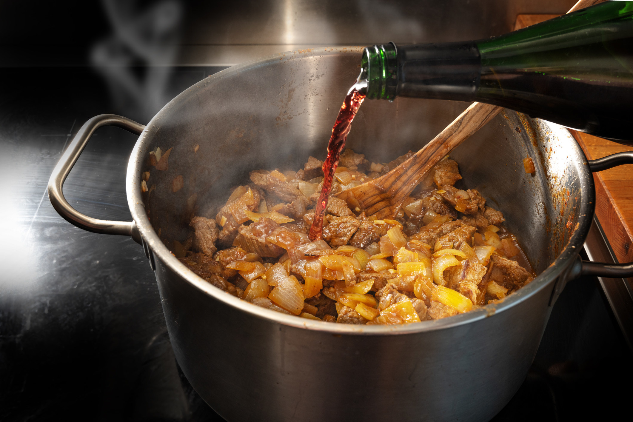 Pouring red wine into a pot of goulash.