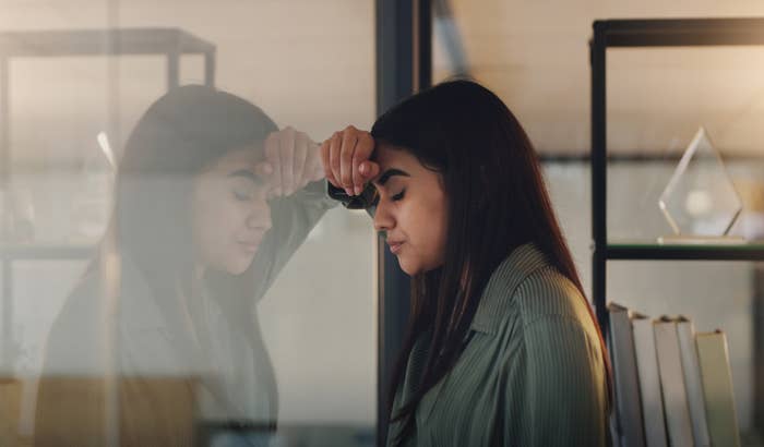 Person leaning against an office window looking pensive