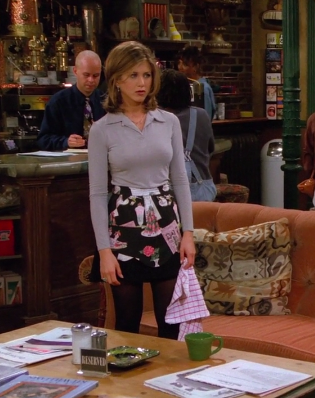 Rachel wearing small booties, tights, a skirt, an apron, and a long-sleeve shirt with a collar like a blazer