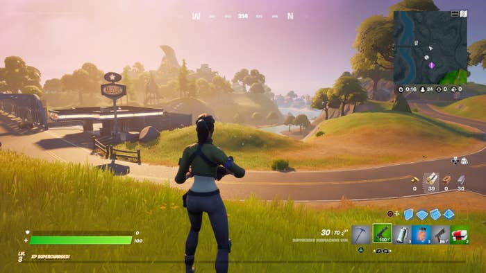 A Fortnite character standing in the middle of the field; they are equipped with a gun and you can see other controls like their health bar and inventory