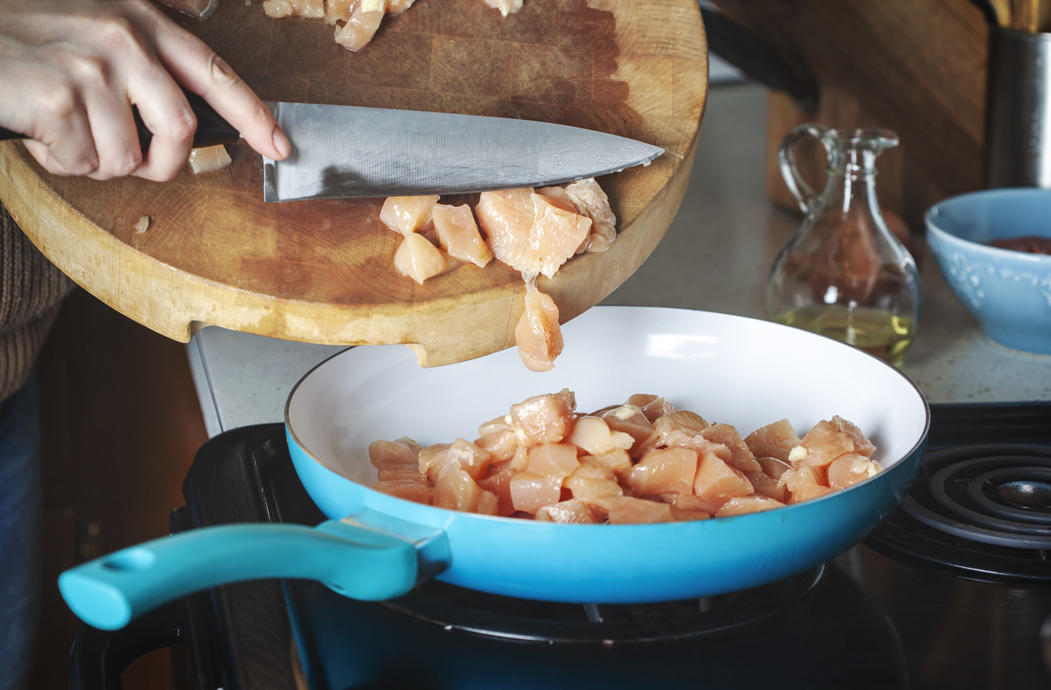 A woman putting diced chicken into a skillet.