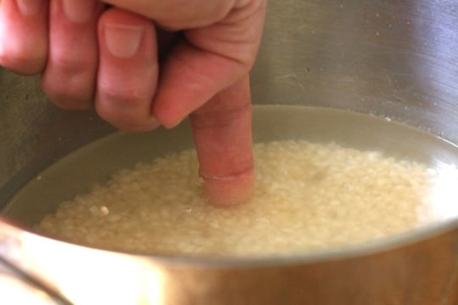 Someone sticking a finger into a pot of rice.