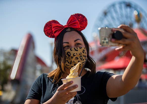 Woman in Mickey Mouse ears taking a selfie in Disney theme park.