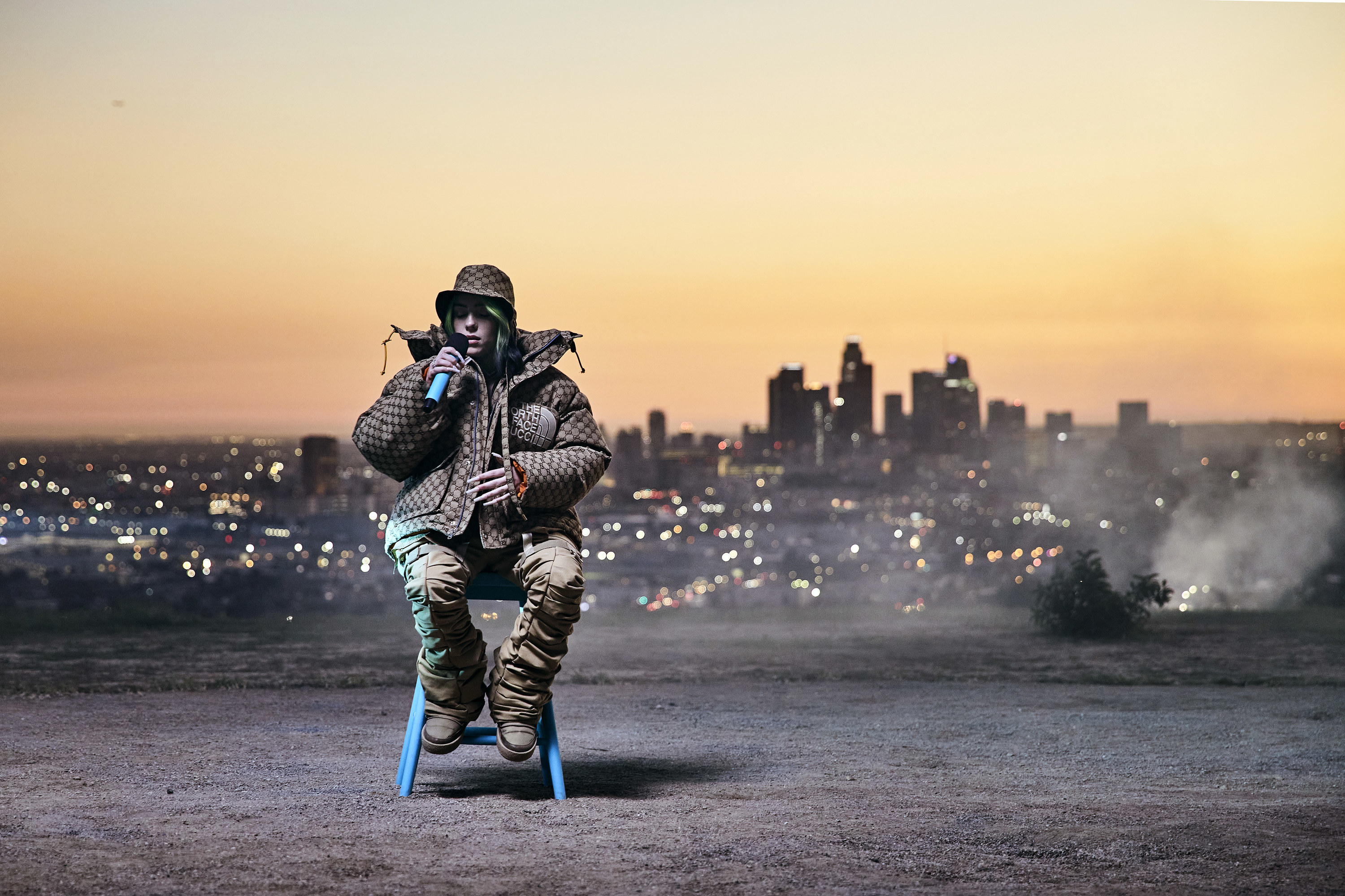 Billie performing outside with a cityscape in the background