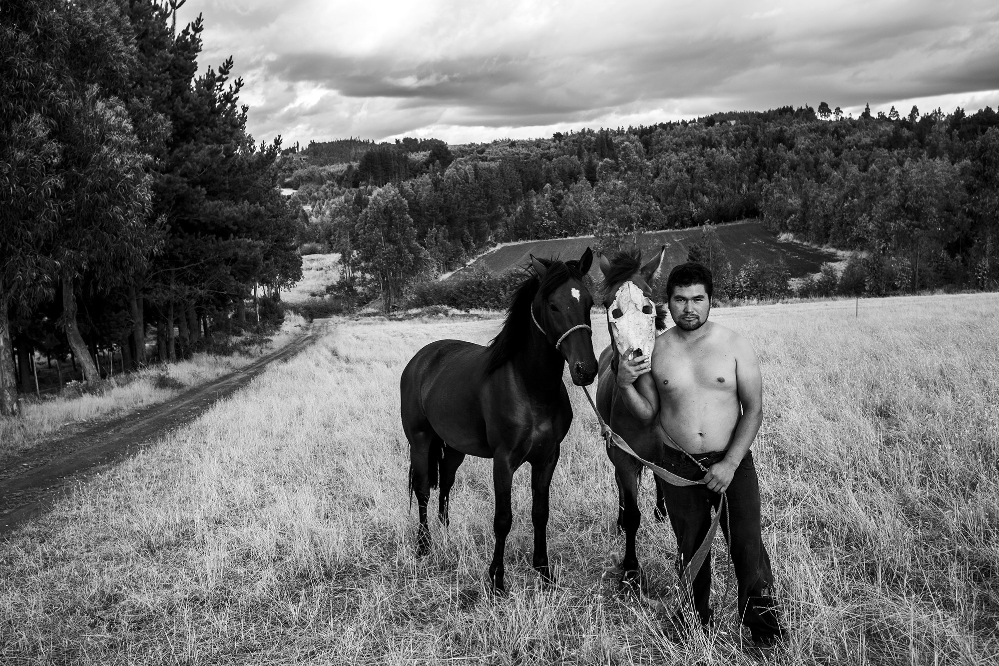 A man stands with two horses in a black-and-white photo