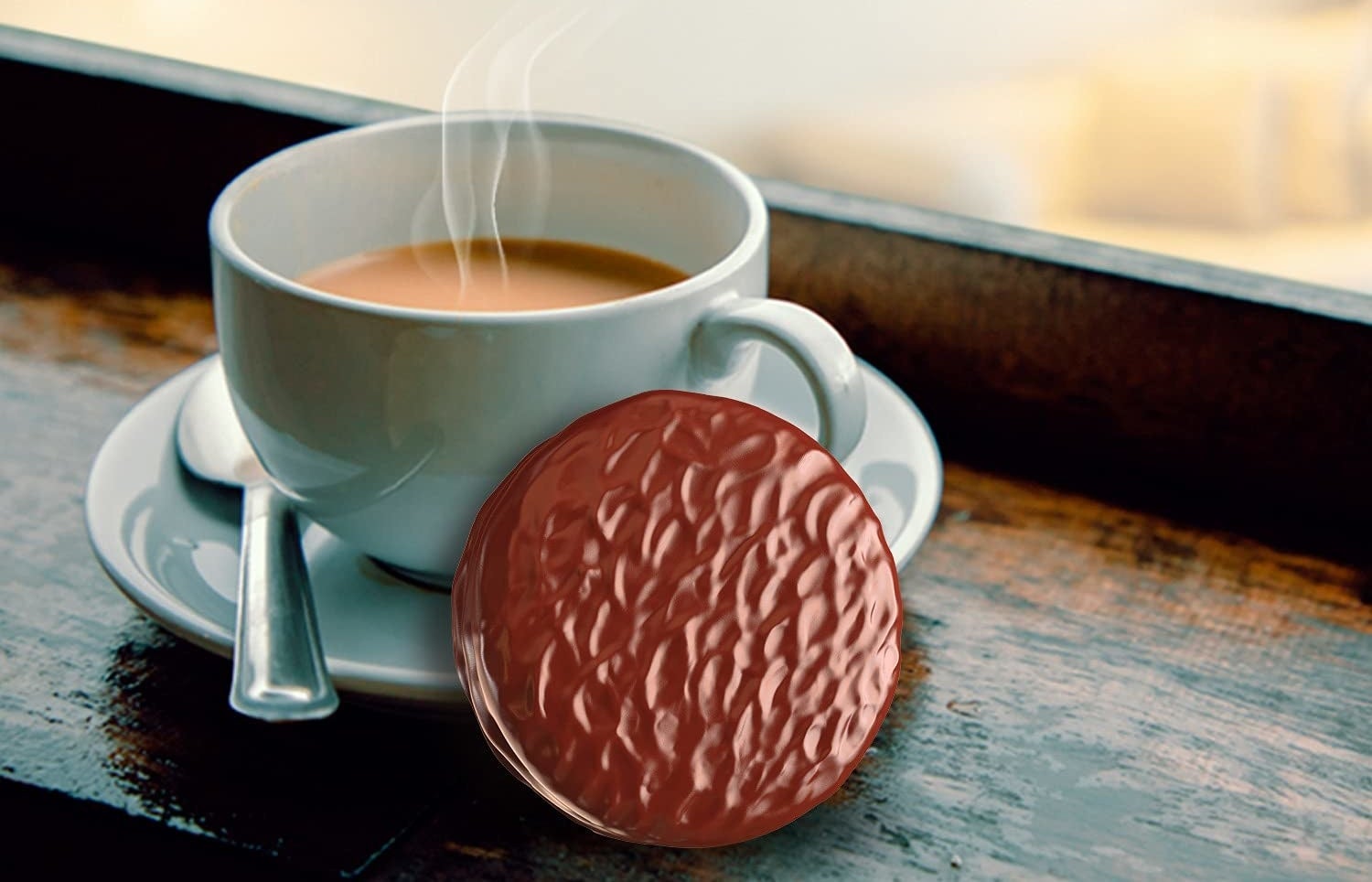 A piece of choco pie kept beside a steaming cup of chai