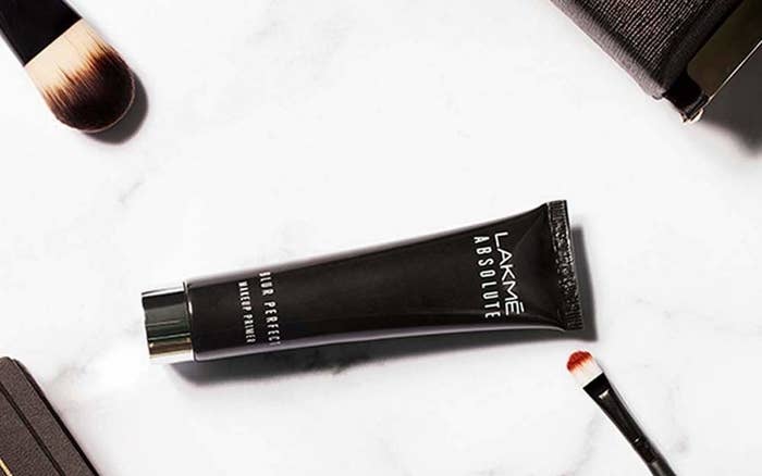 A tube of Lakmé Absolute blur perfect makeup primer in black with makeup brushes kept beside it