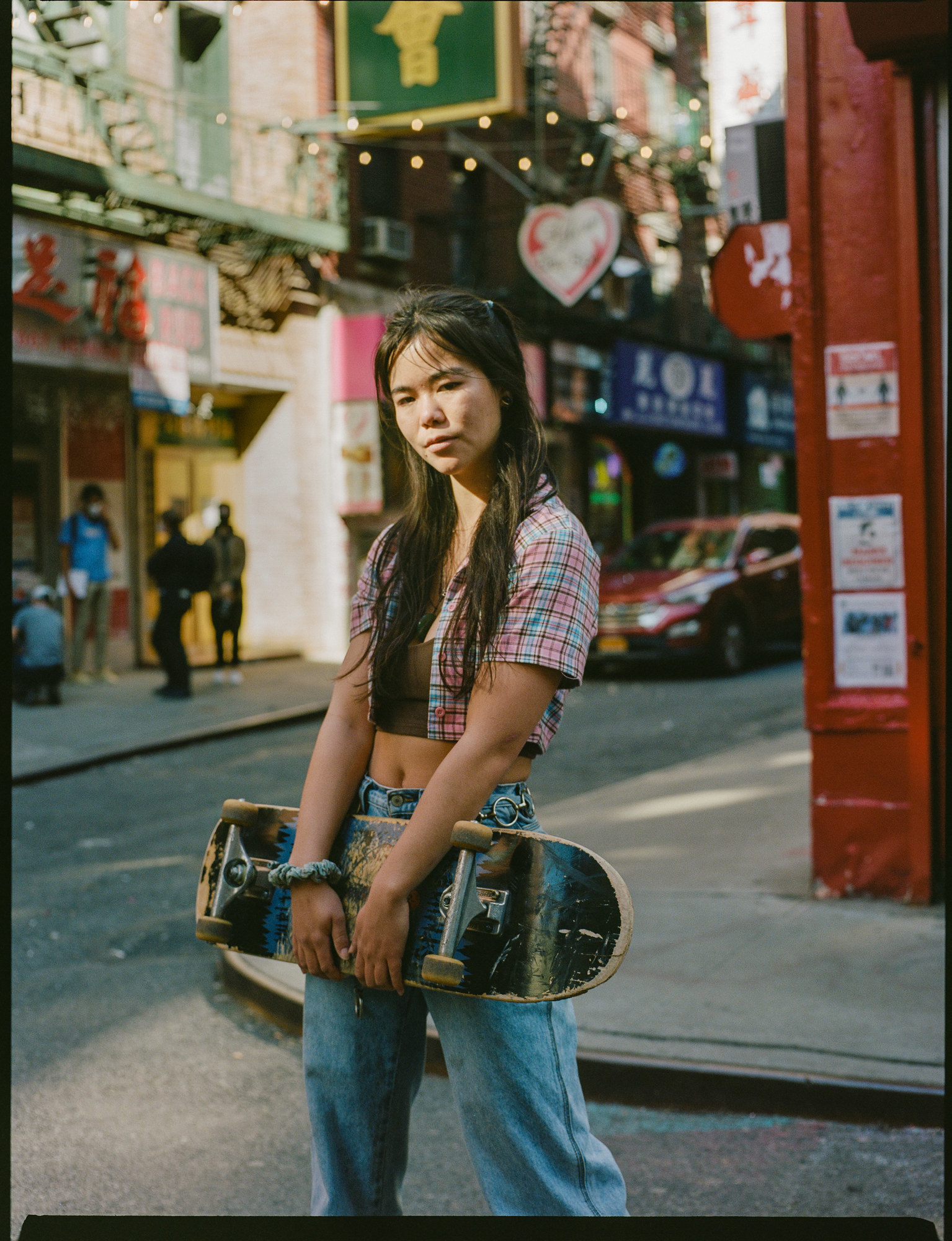 A woman in a crop top and jeans holds a skateboard