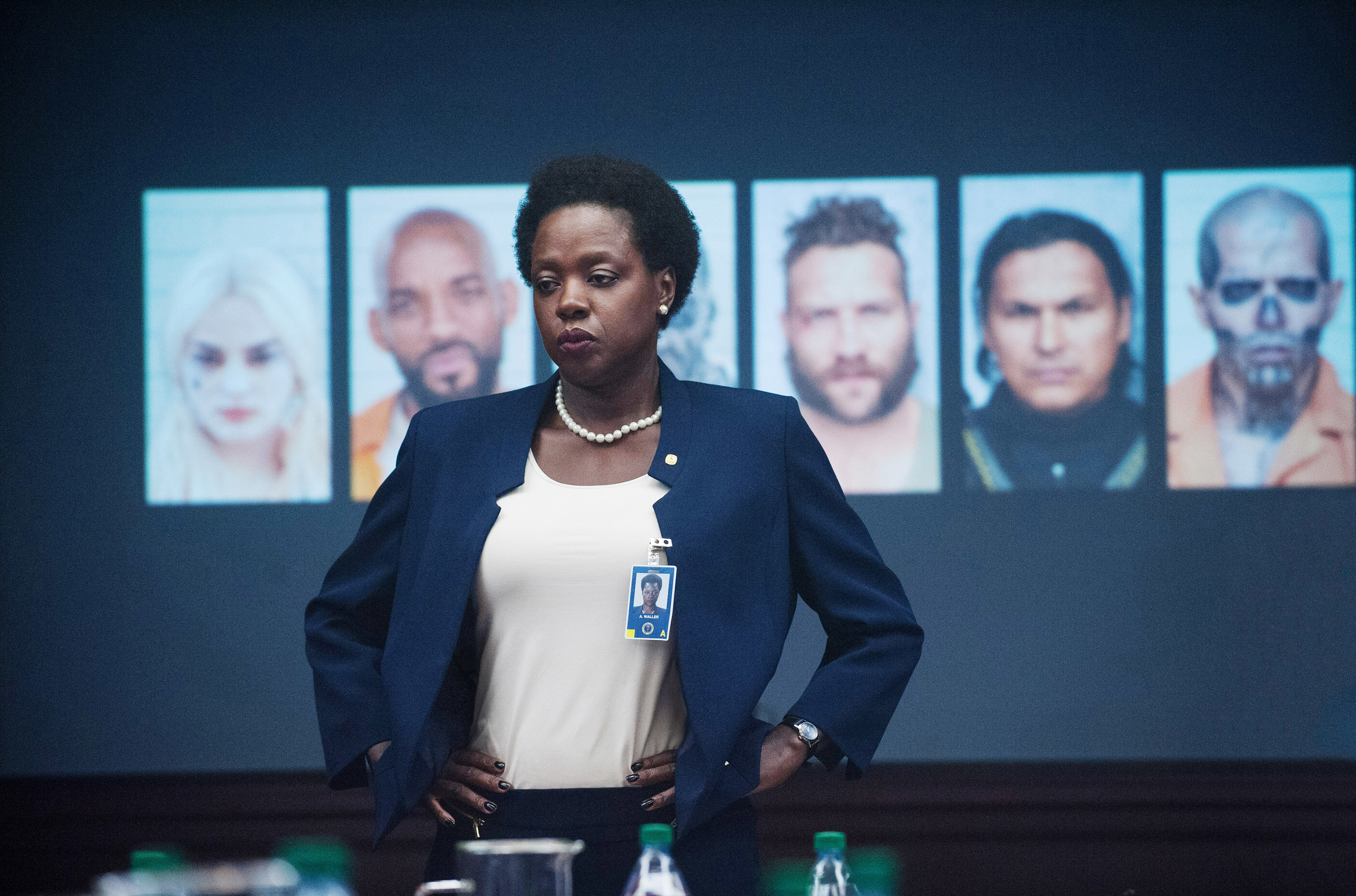 Viola Davis as Amanda Waller standing in a room with pictures of the Suicide Squad projected behind her