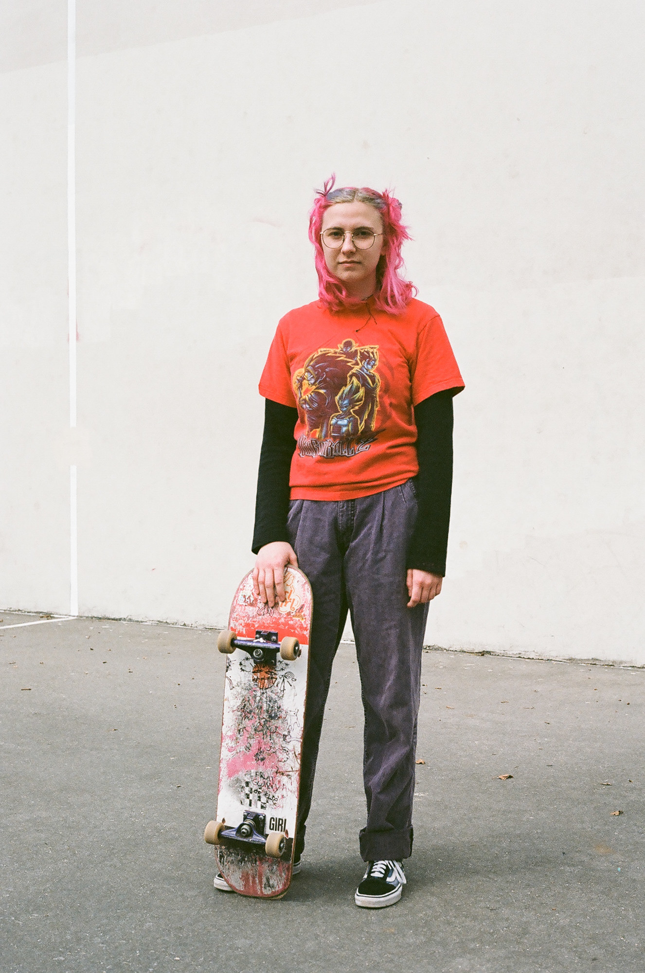 A woman with pink hair stands with a pink skateboard