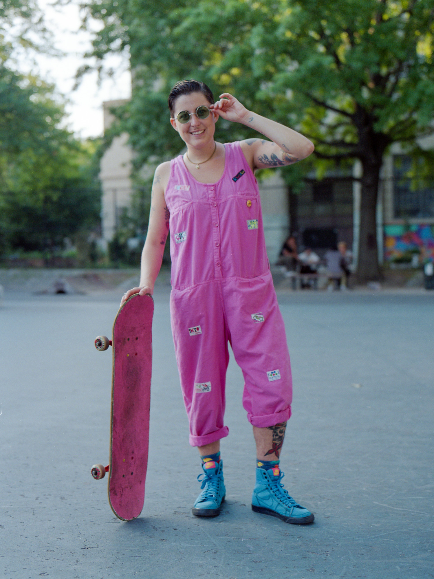 A woman in an all pink romper with blue sneakers and a skateboard that is painted pink