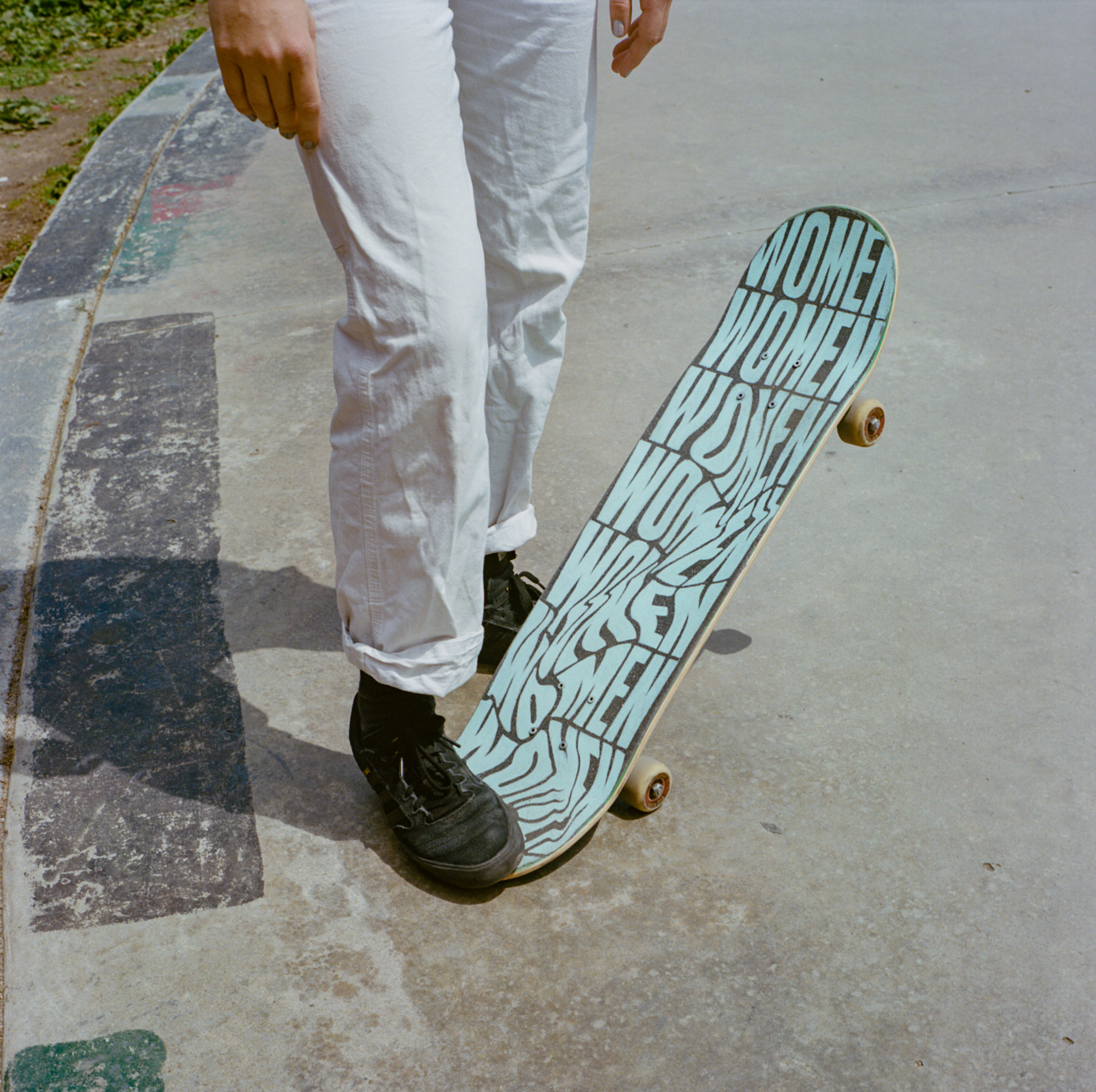 A woman with one foot on a skateboard that says &quot;women&quot; all over it