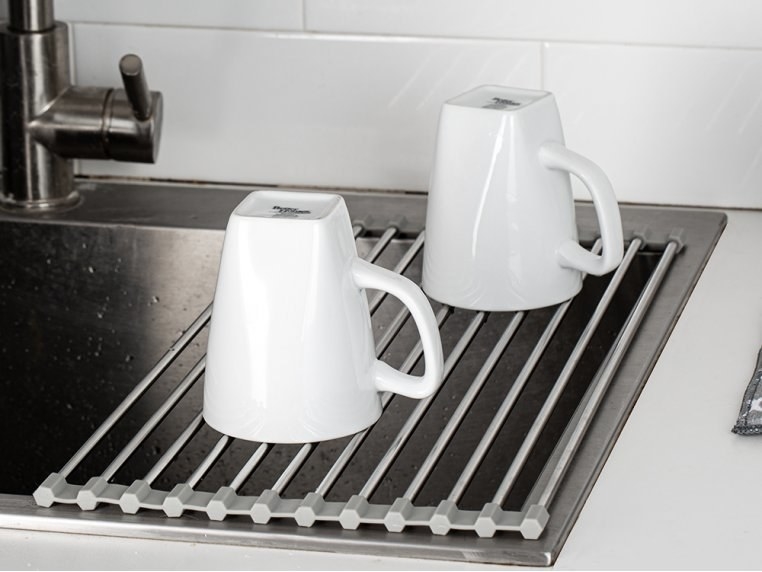 The stainless rack over part of a sink with mugs drying on it
