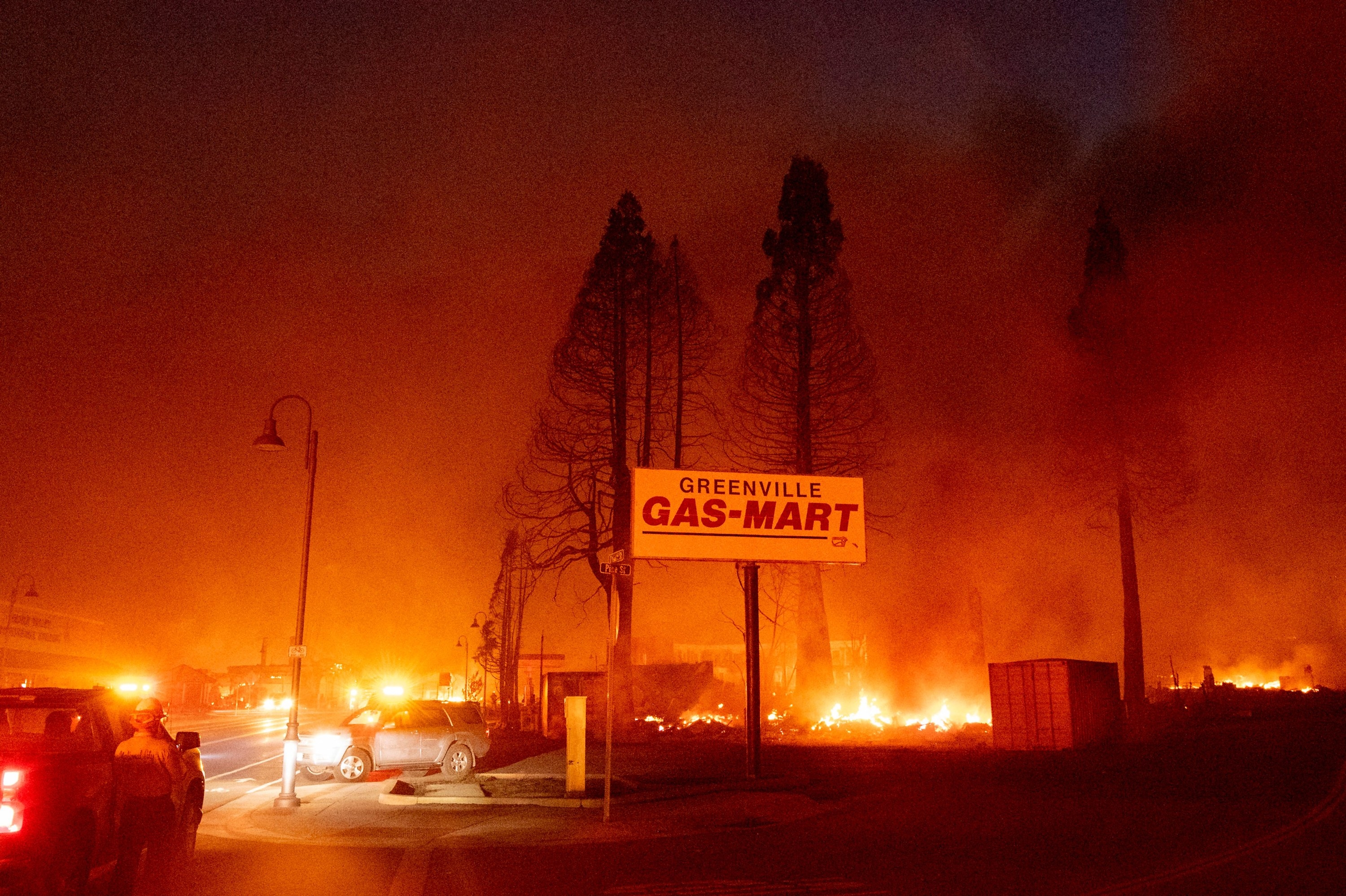 A sign for Greenville Gas Mart is surrounded by a fire under a smoky sky