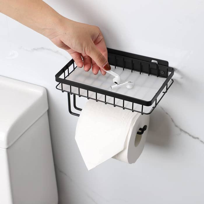 A person putting their AirPods into the tray above a roll of toilet paper