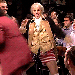 A man dressed as George Washington and wearing short USA shorts dances