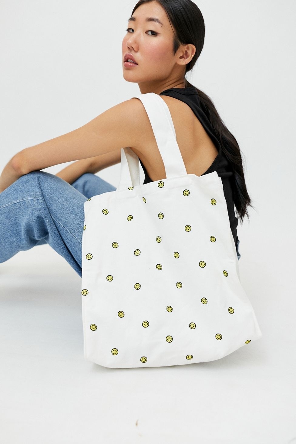 a model holding a white tote with embroidered smiley faces all over it