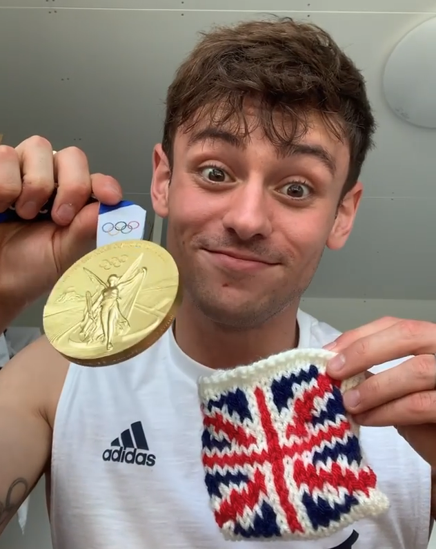 Tom Daley holding his Olympic medal and the pouch he knitted for it