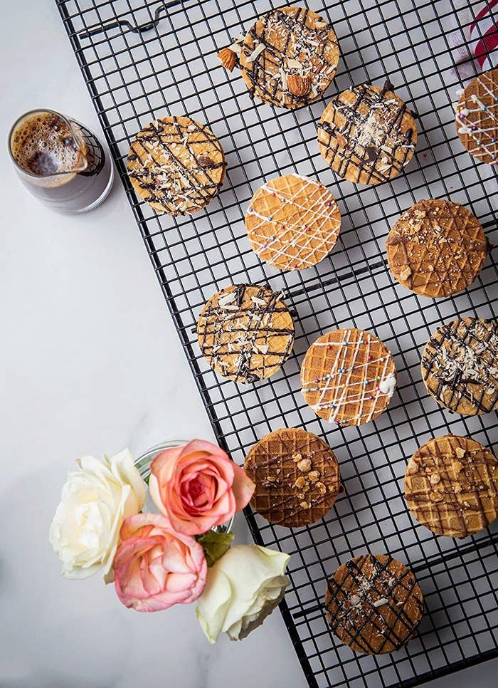 Different flavours of assorted mini waffle cookies kept on a black mesh rack along with a jar of black coffee