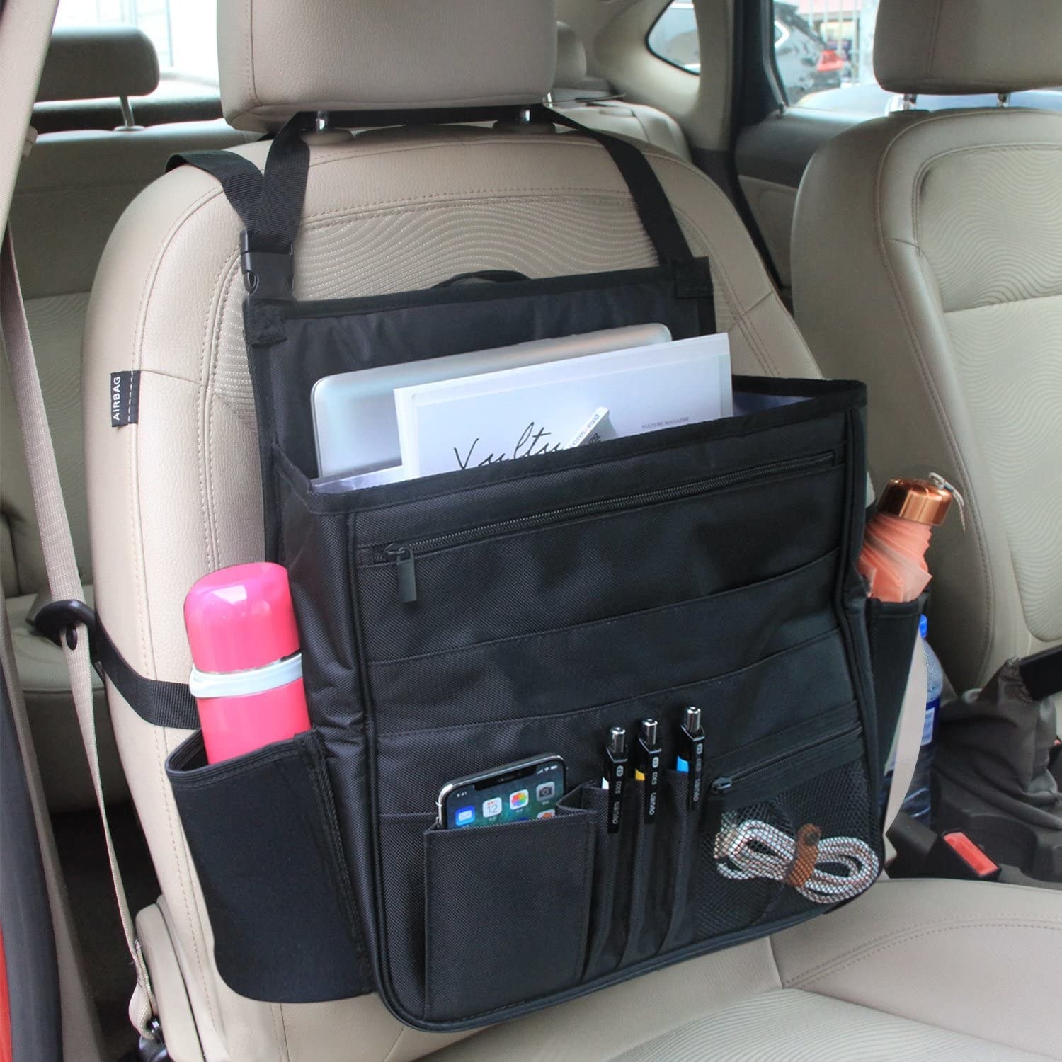 Several items, including pens, a phone, and a computer, in the passenger seat organizer