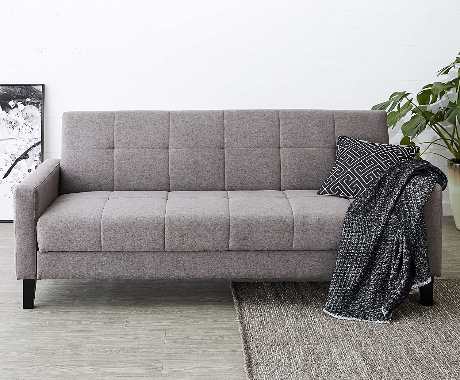 A grey sofa with a pillow and a blanket on it
