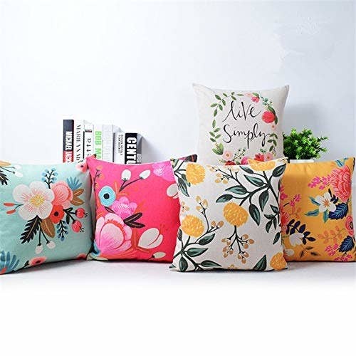 5 floral cushion covers in yellow, pink, white and blue colours placed with some books and indoor plants behind them