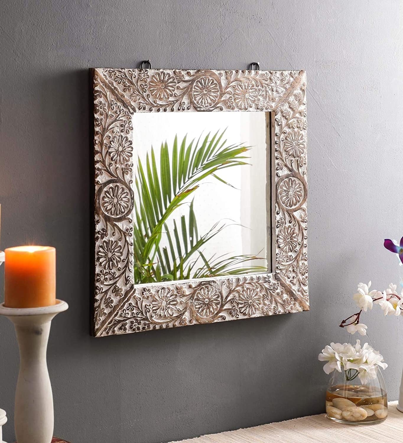 White and burnt brown polished framed square mirror hanging on a grey wall with a table holding a candle and a potted plant underneath