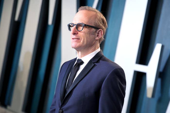 Bob posing for photographers on the red carpet in a suit and glasses