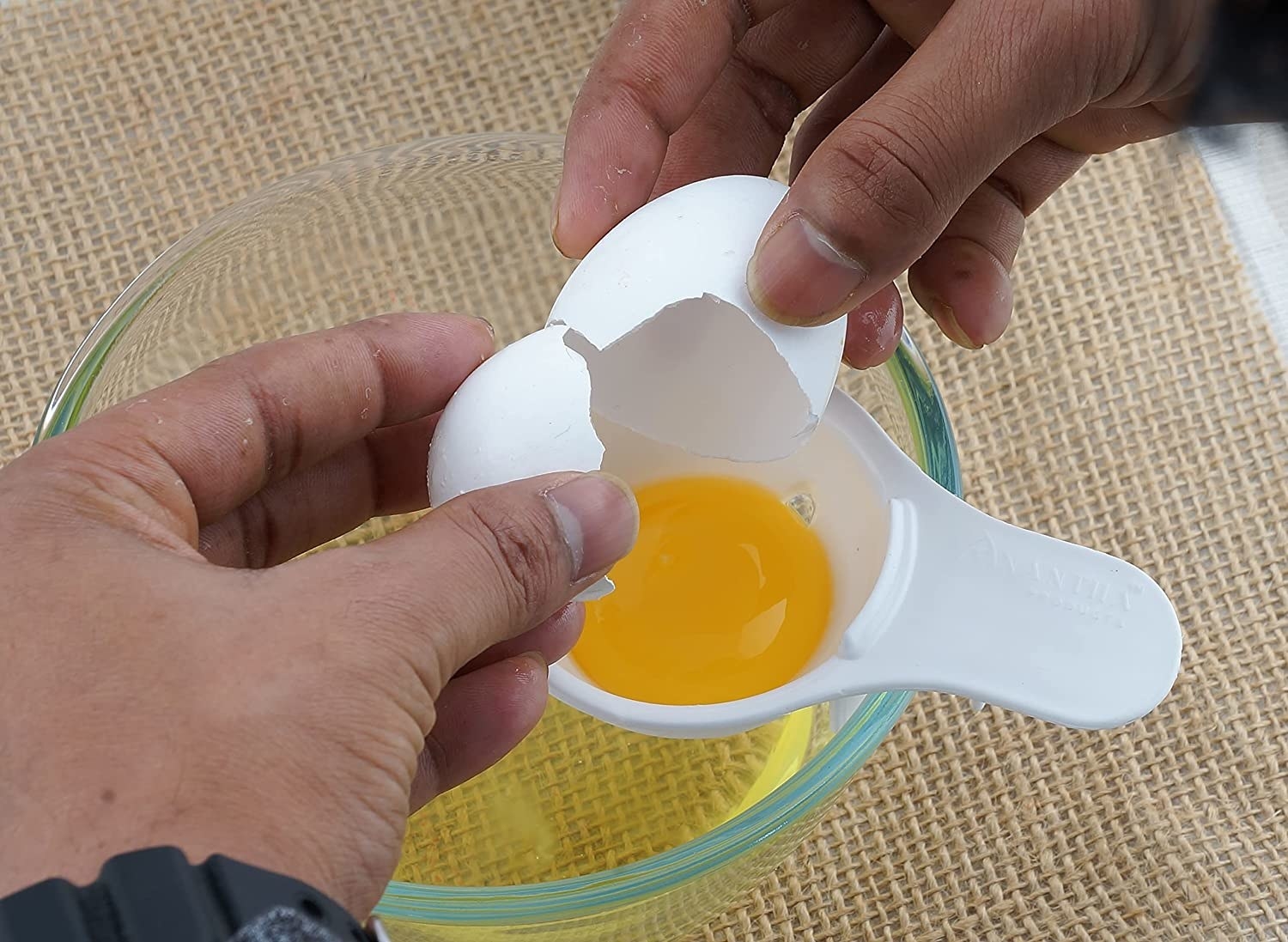 A person breaking an egg on top of the egg white separator placed on a bowl