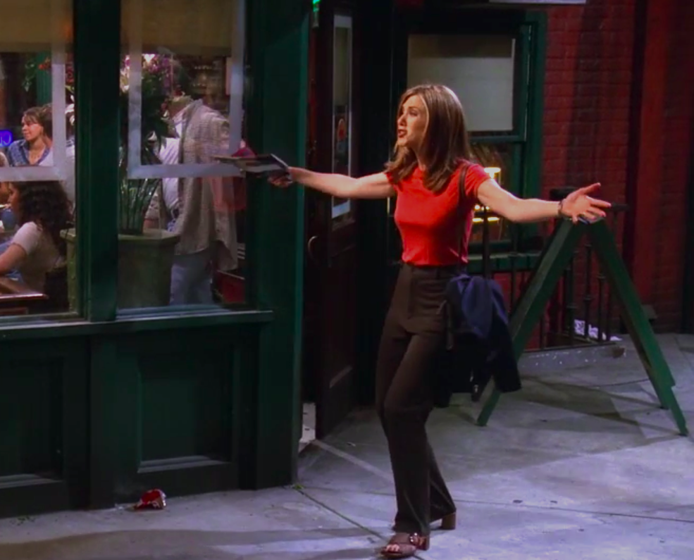 Rachel wearing slim pants, a red shirt, and a cute off-the-shoulder bag, but also weird sandal heels