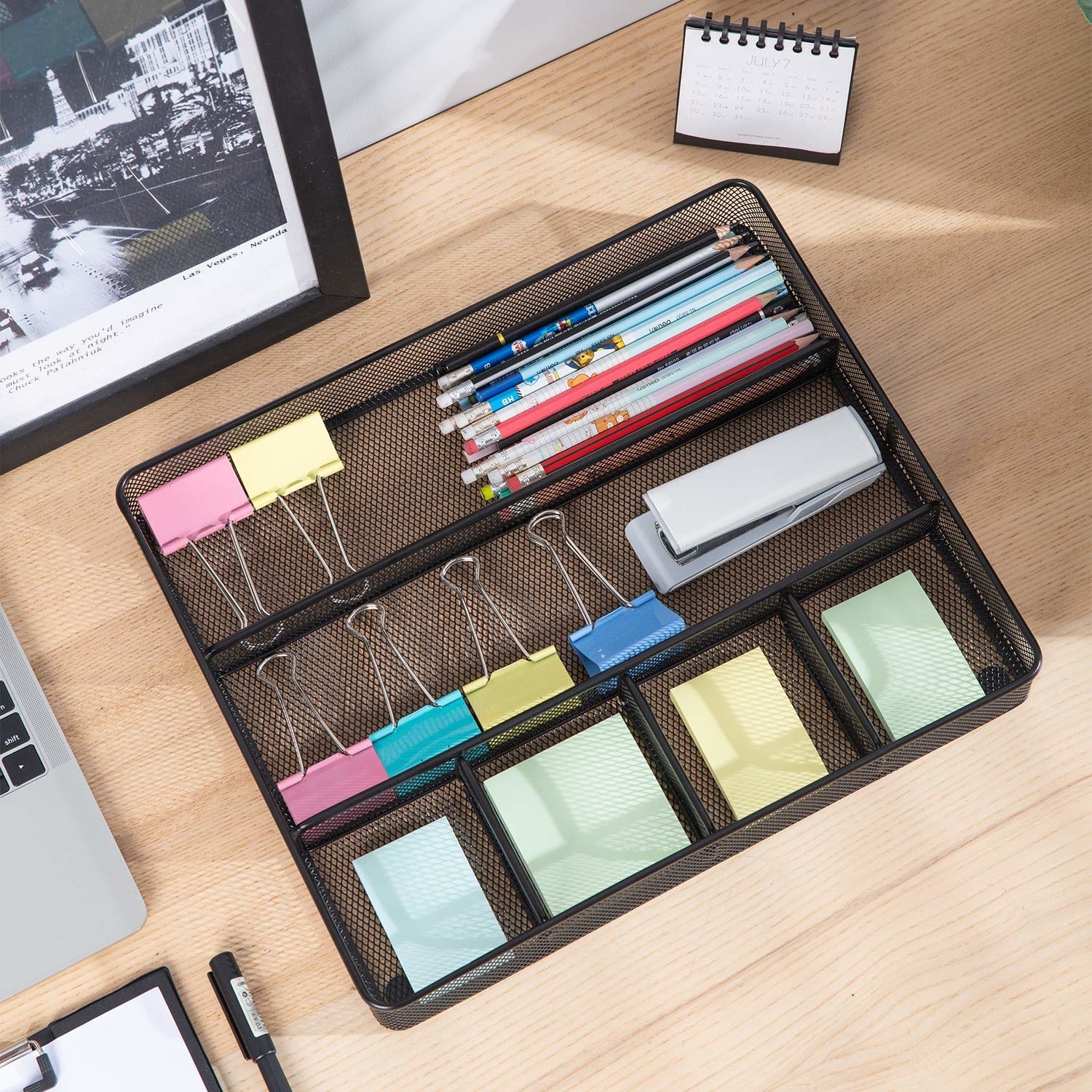 A mesh organiser on a desk with multiple stationery items in it