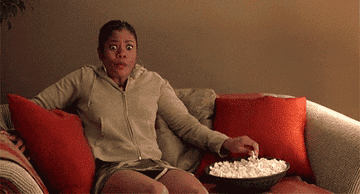 Person sitting on a couch and eating popcorn  and looking excited