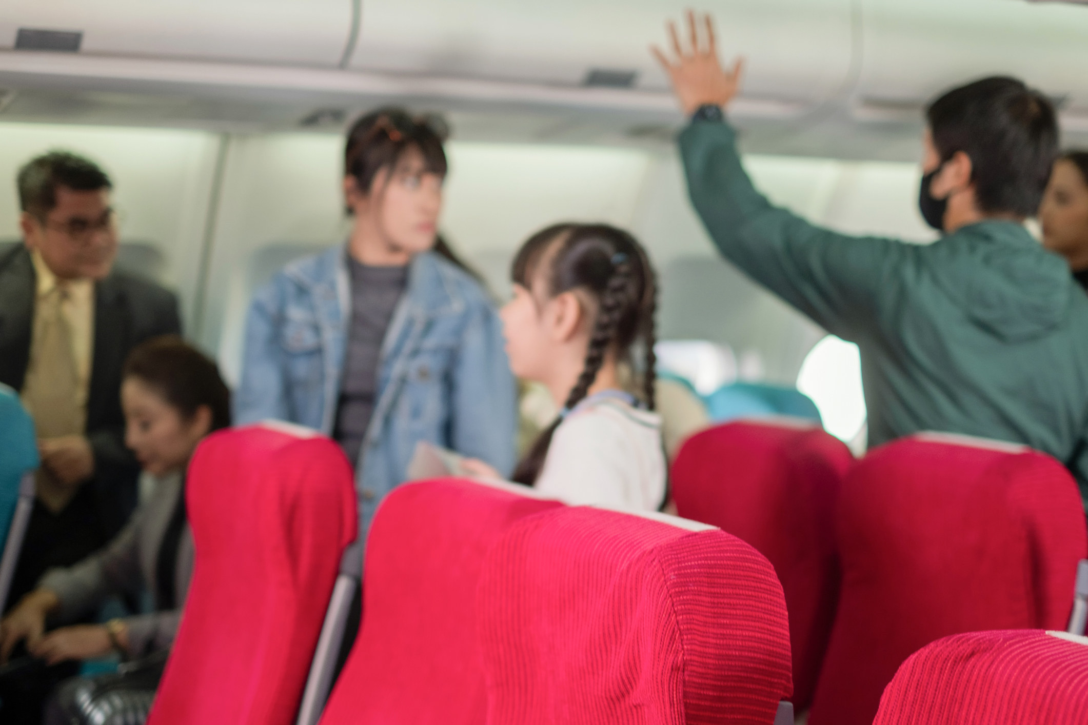 People stand up on an airplane and reach for the overhead compartment