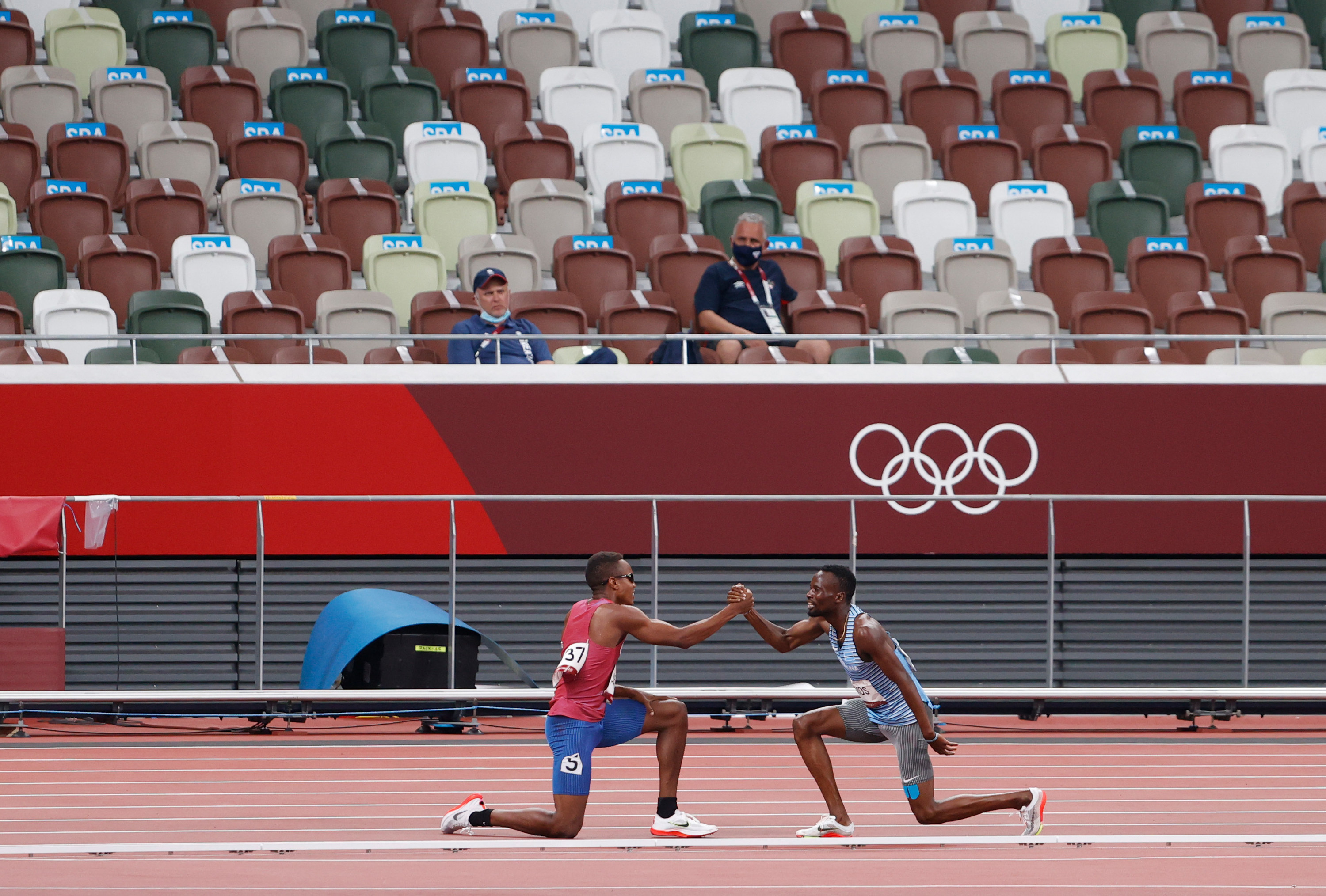 Isaiah and Nijel kneel on one knee and clasp hands on the track