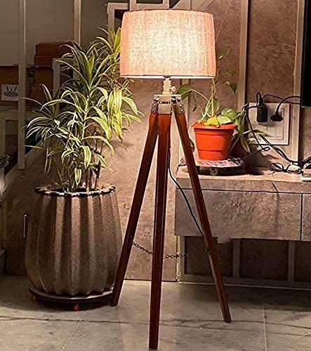 A tripod shaped lamp made from teak wood and beige lampshade