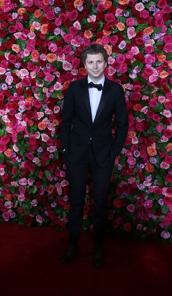迈克尔·塞拉穿着黑色晚礼服站在墙前面的玫瑰在第72届托尼奖