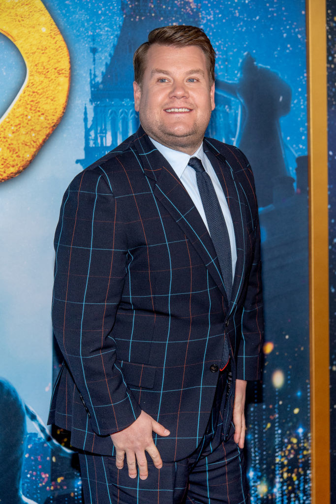 James Corden smiling and standing with his hands resting on the tops of his thighs