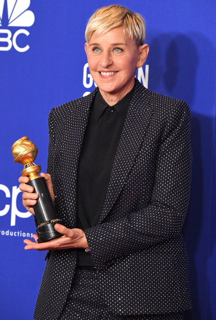 Ellen DeGeneres smiling and holding an award on the red carpet