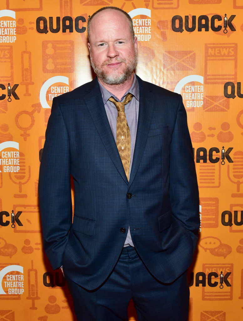 Joss Whedon on the red carpet in a suit and tie and hands in pockets