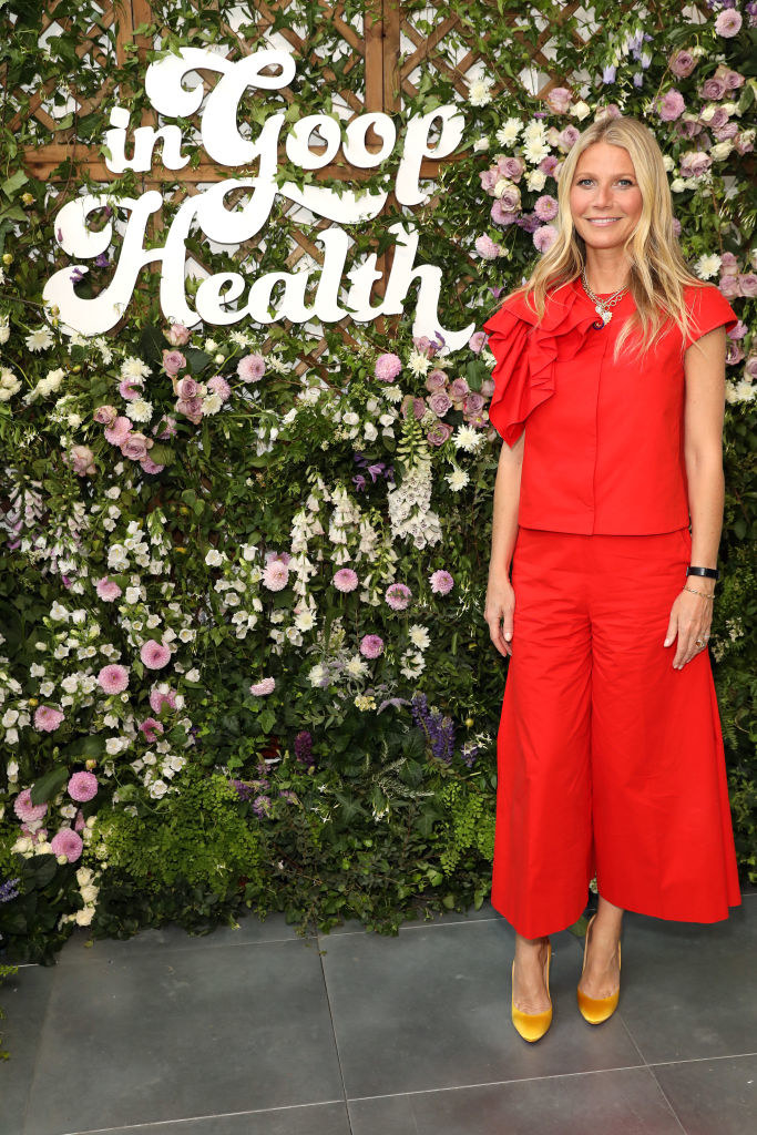 A smiling Gwyneth Paltrow standing near a sign reading &quot;In Goop Health&quot;