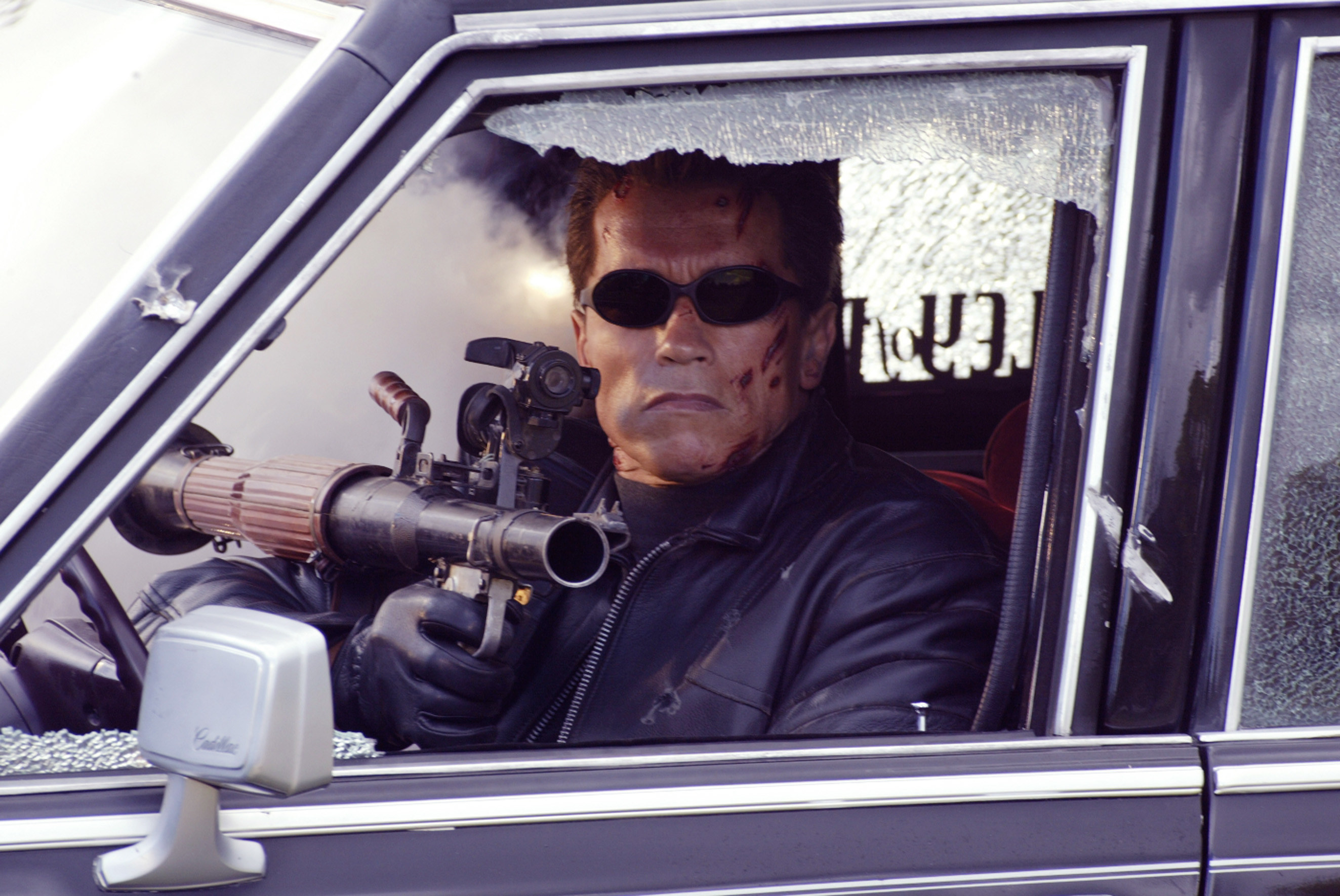 the Terminator with a gun in the driver&#x27;s seat of a car with a smashed window