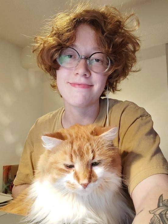 Kira Fennell smiles at the camera in a selfie with their cat