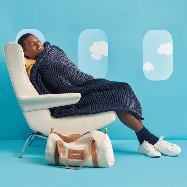 model sitting in a chair that looks like an airplane seat with a navy blue knitted blanket over them