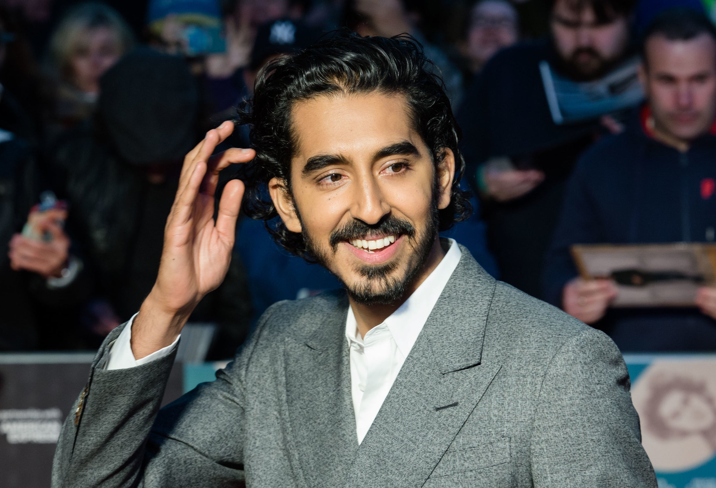 Photo of Dev Patel in a gray suit smiling at something off-camera